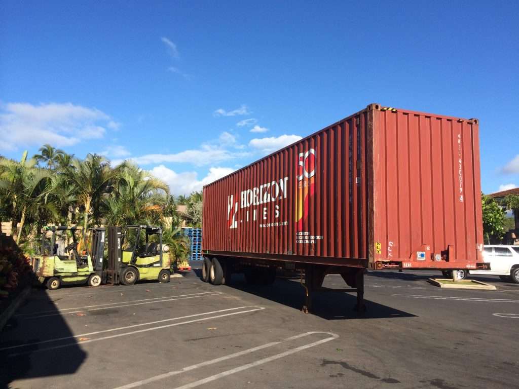 40ft shipping container on a chassis trailer in a parking lot in Hawaii, with forklifts and palm trees
