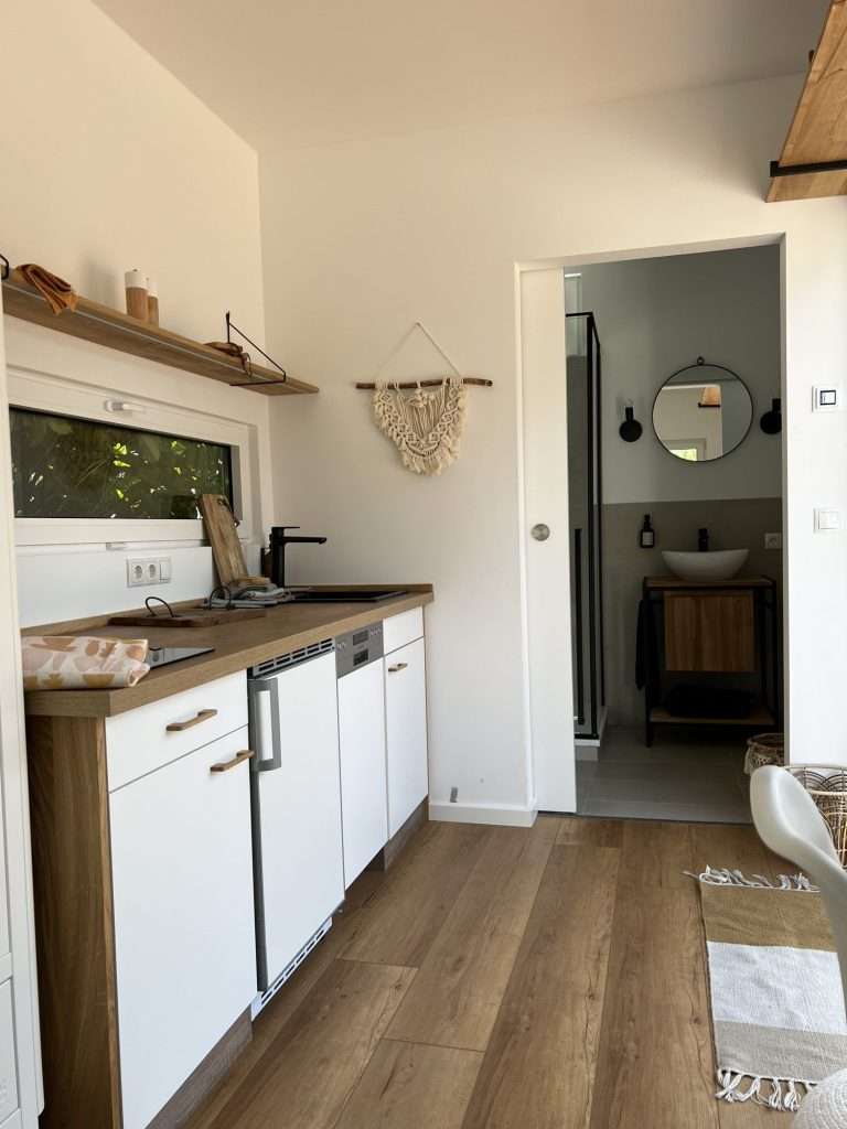 Kitchenette and bathroom door inside a small container home with a wood floor