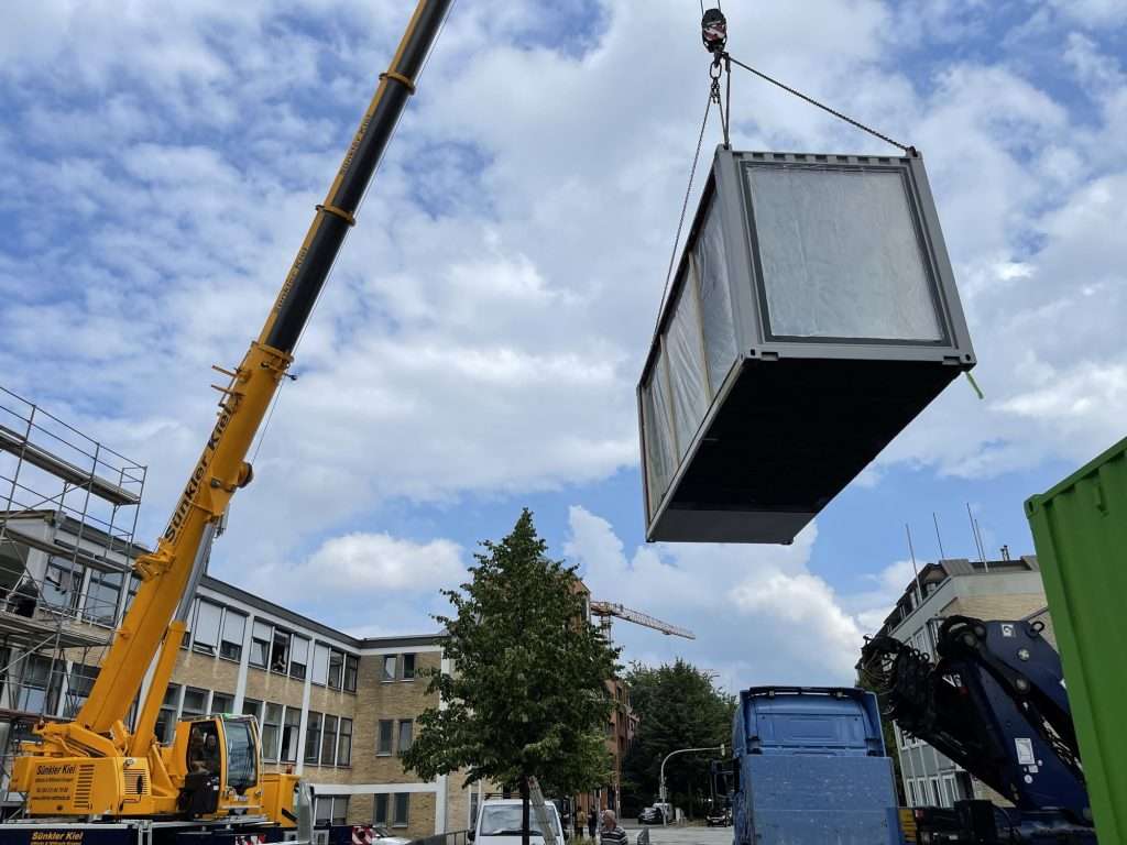 Mobile crane lifting a container module next to a building
