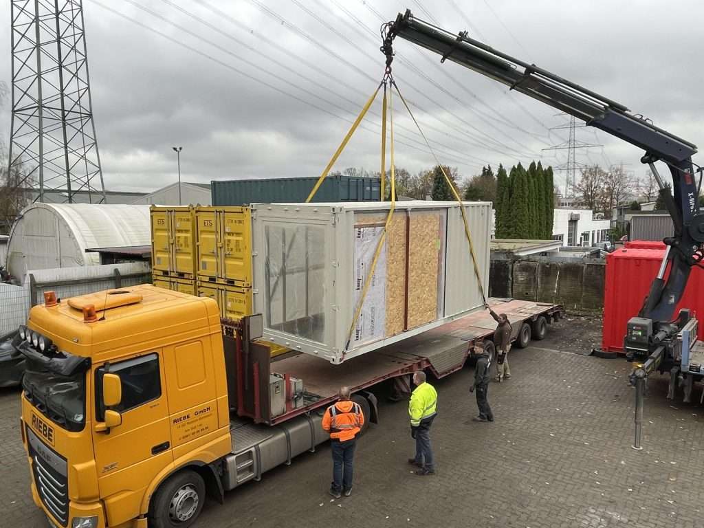 Truck with a loader crane unloading a finished container module